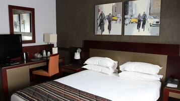 Een hotelkamer met een bed, een bureau met een computer, een stoel, een televisie en kunst aan de muur.