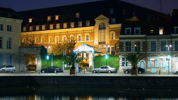 A waterfront hotel with a prominent building featuring arched windows and a well-lit entrance.