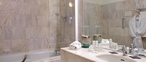 Ein modernes Badezimmer mit einer Duschkabine aus Marmor, einer Badewanne, einem großen Spiegel und einem Waschtisch mit Pflegeprodukten.