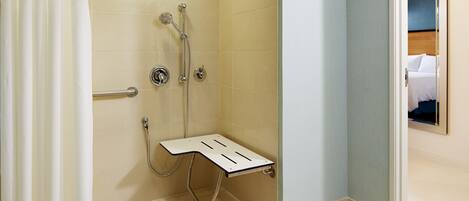 Une salle de bain moderne équipée d’une douche, d’une barre d’appui et d’un petit banc.