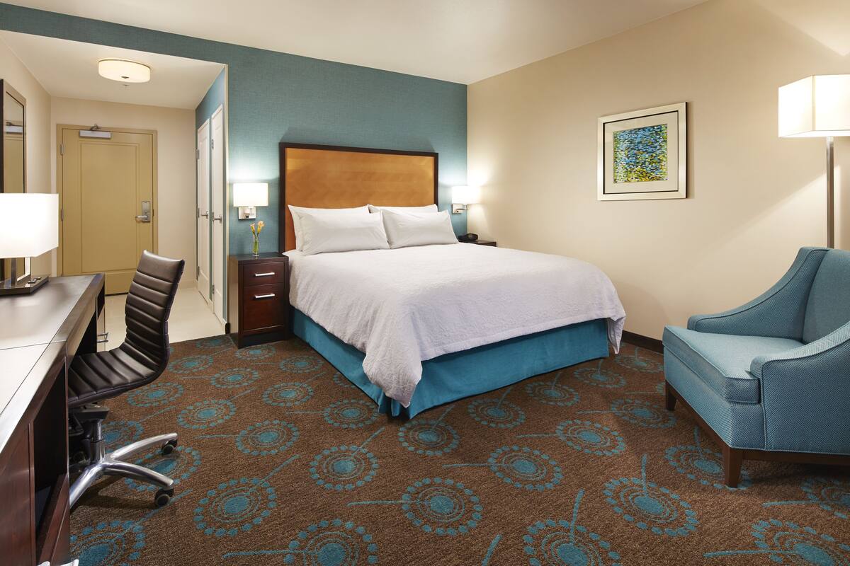 A hotel room with a bed, a desk, a chair, and a lamp.