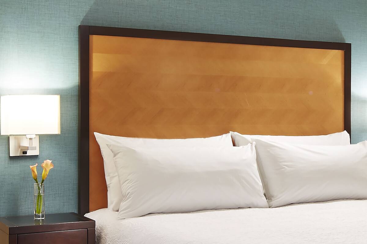 A hotel room with a large bed, white pillows, a nightstand with a lamp, and a vase with flowers.