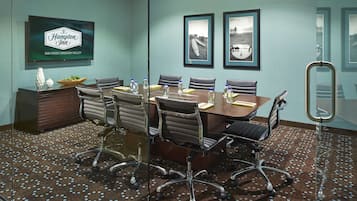 A conference room with a large table, six chairs, a television displaying 'Hampton Inn San Diego/Mission Valley', and framed pictures on the wall.