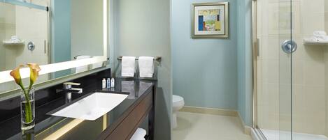 Un baño moderno con encimera negra, lavabo blanco y cabina de ducha con mampara de vidrio.