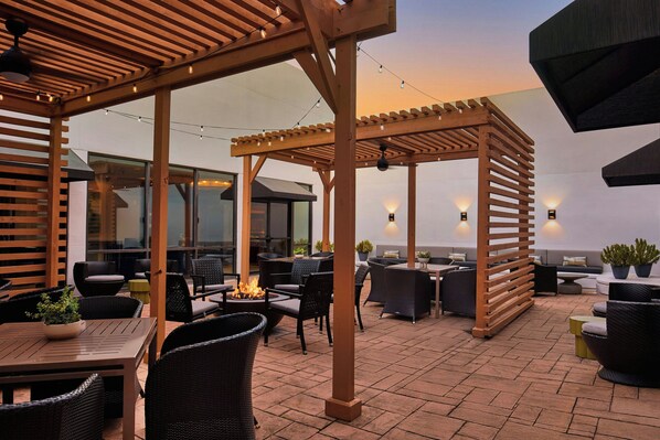 Un área de patio al aire libre con pérgolas de madera, mobiliario de mimbre y una chimenea.