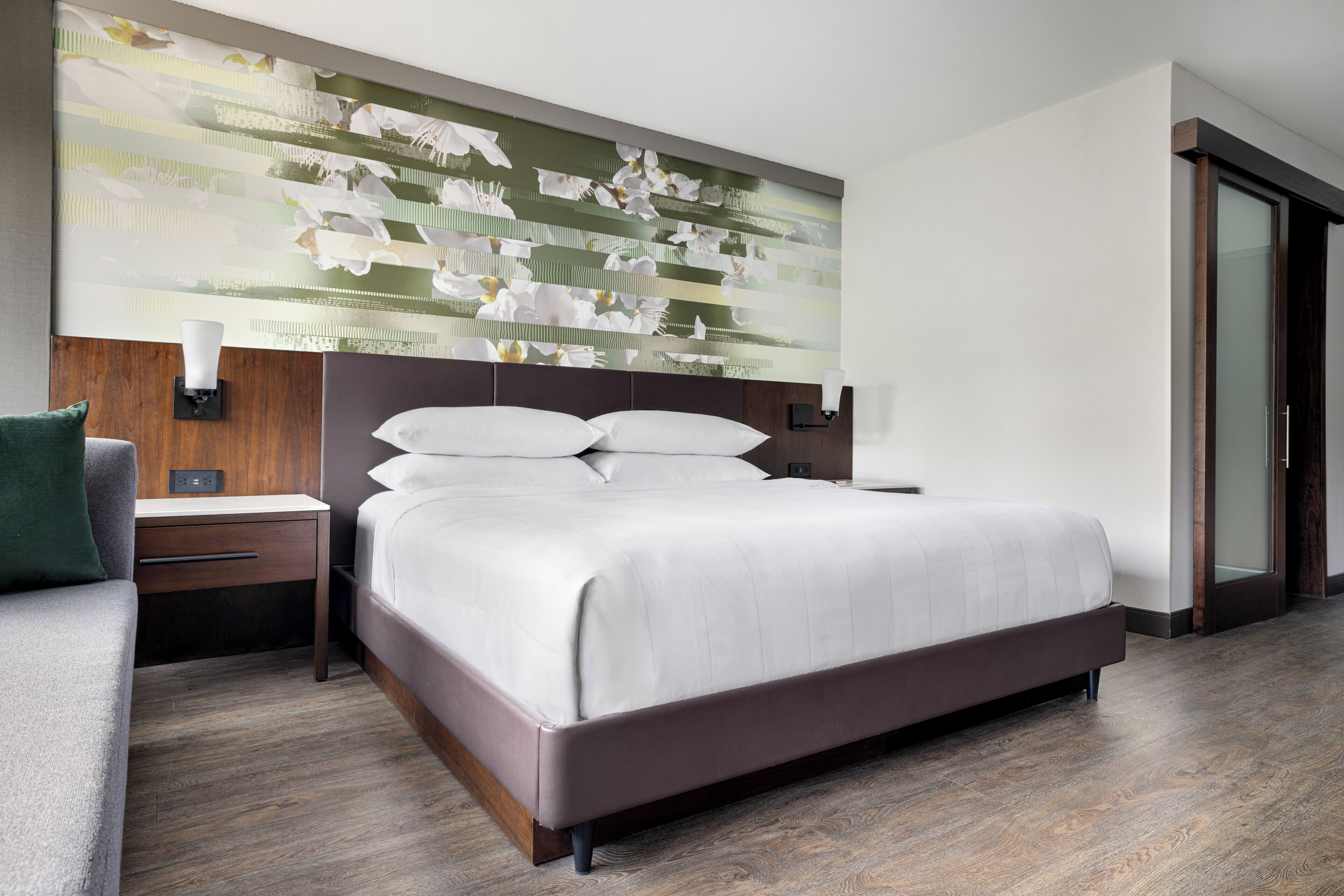 A modern hotel room with a large bed, a nightstand, a wall-mounted lamp, and a decorative wall art piece.