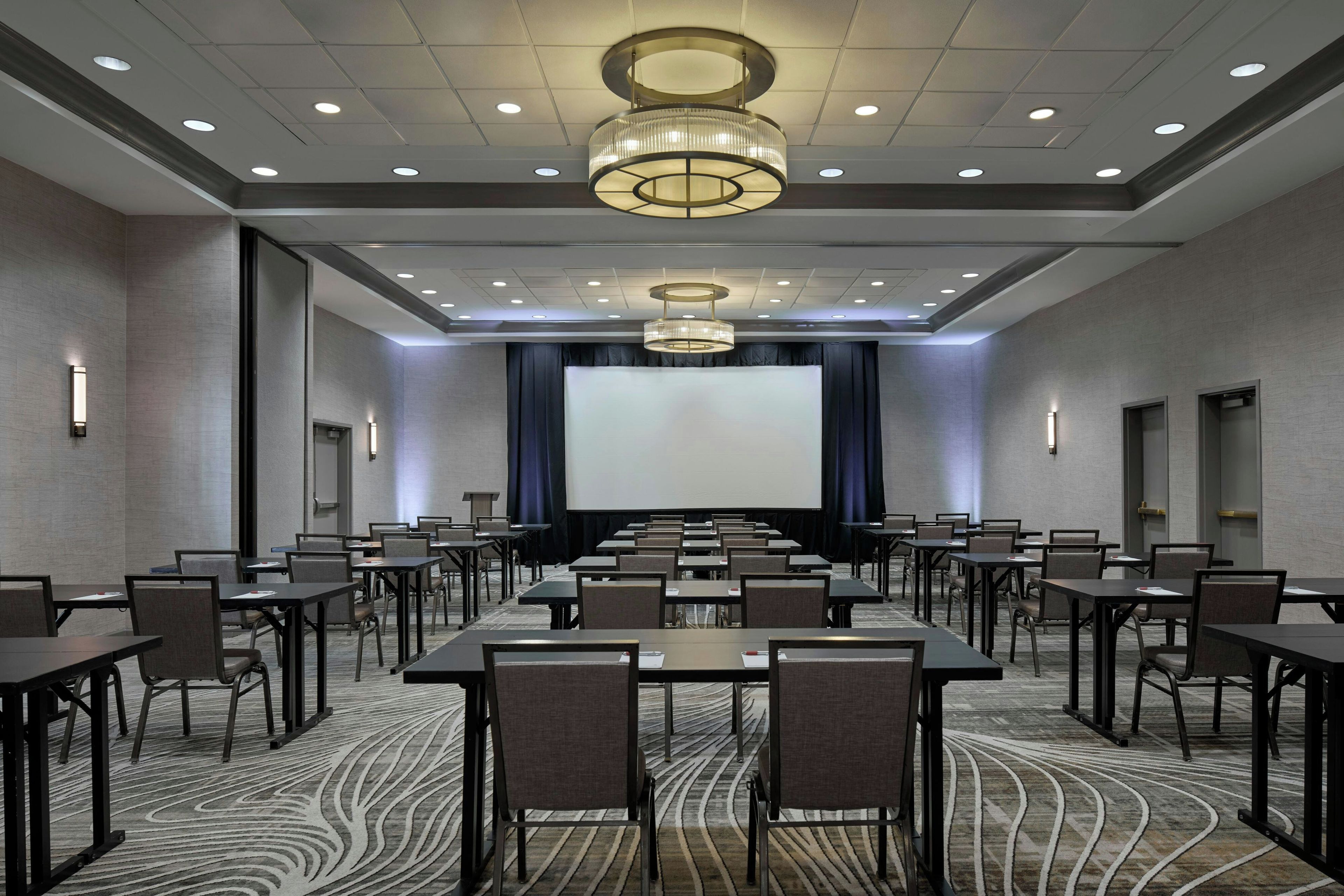 A conference room with a large screen, multiple tables, chairs, and a patterned carpet.