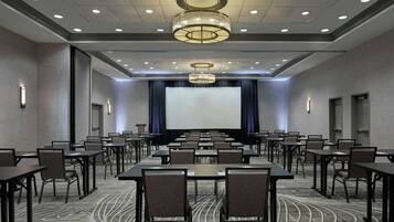 A conference room with a large screen, multiple tables, chairs, and a patterned carpet.