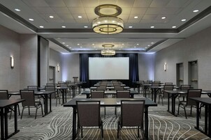 A conference room with a large screen, multiple tables, chairs, and a patterned carpet.