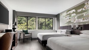 A hotel room with two beds, a desk, a chair, and a large window with a view of trees. - Atlanta Marriott Peachtree Corners (Peachtree Corners)