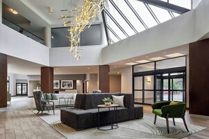 Um hall espaçoso com teto alto, um lustre moderno, um sofá de canto e uma poltrona verde.
