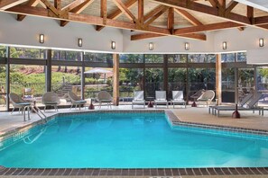 An indoor swimming pool with clear glass walls, wooden beams, and lounge chairs. - Atlanta Marriott Peachtree Corners (Peachtree Corners)