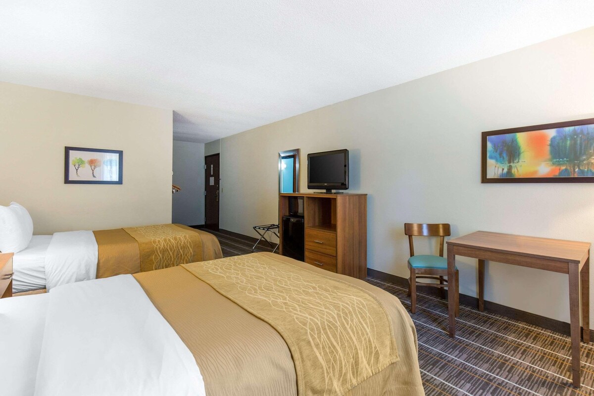 A hotel room with two beds, a desk, a chair, a television, and artwork on the walls.
