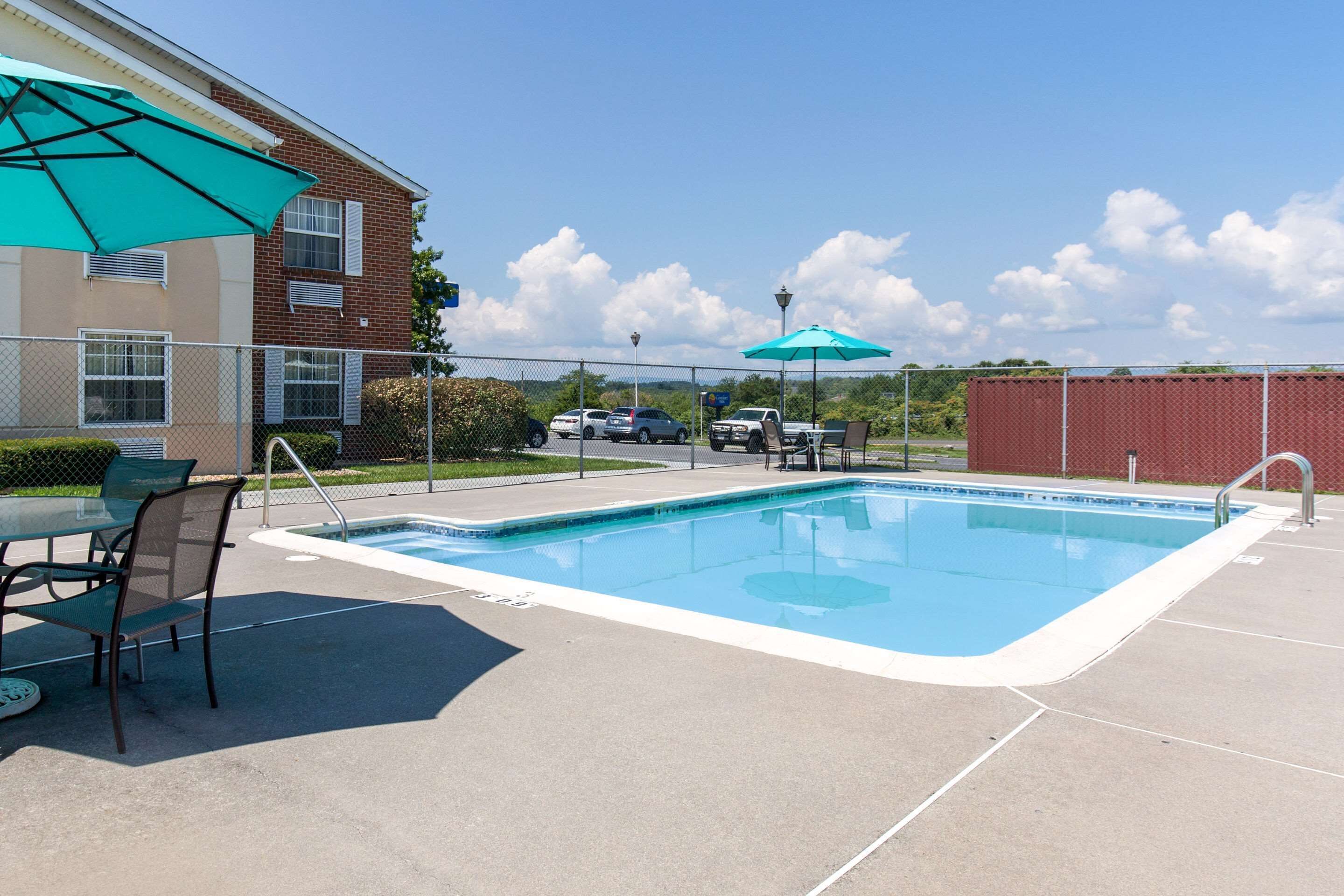 A swimming pool with a tiled deck, a table with chairs, and a green umbrella.