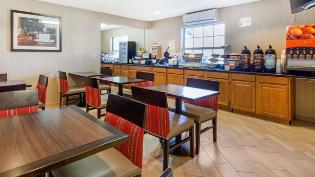 A restaurant with wooden tables and red cushioned chairs, a kitchen area with a coffee machine, and a large window. - Quality Inn Stephens City - Winchester South (Stephens City)