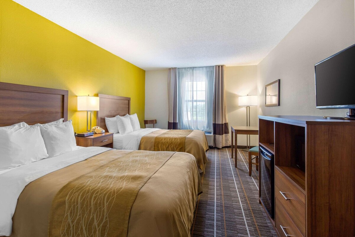 A hotel room with two beds, a desk, a television, and a window with curtains.