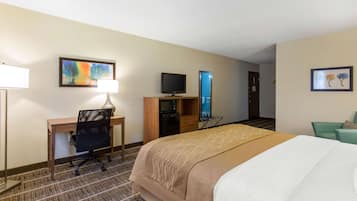 Una habitación de hotel con cama, escritorio, silla, televisor y obras de arte en las paredes.