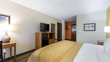 A hotel room with a large bed, a television on a wooden stand, a desk with a lamp, and a door leading to another room.