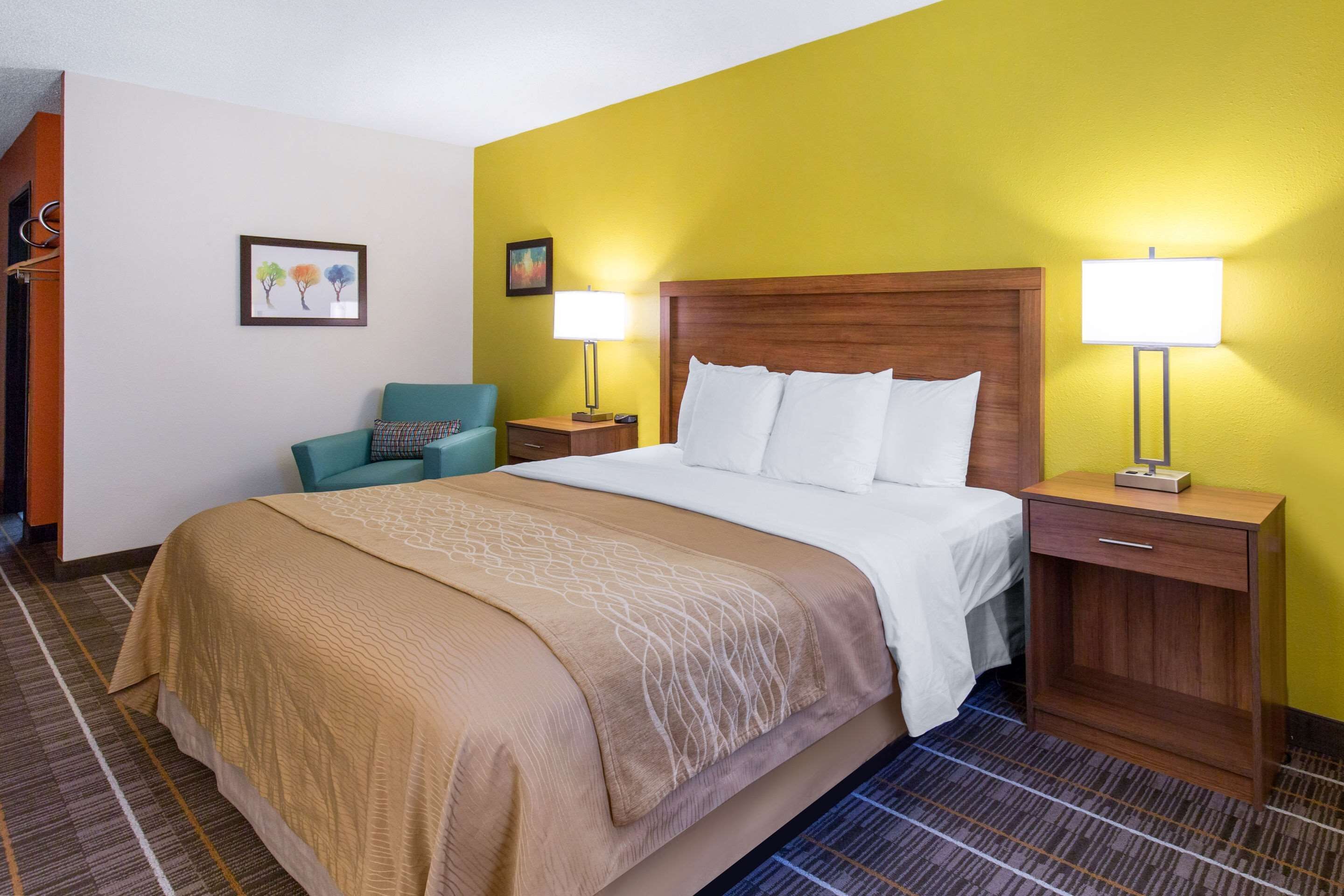 Quarto de hotel com uma cama, duas mesas de cabeceira, uma cadeira e um quadro na parede.