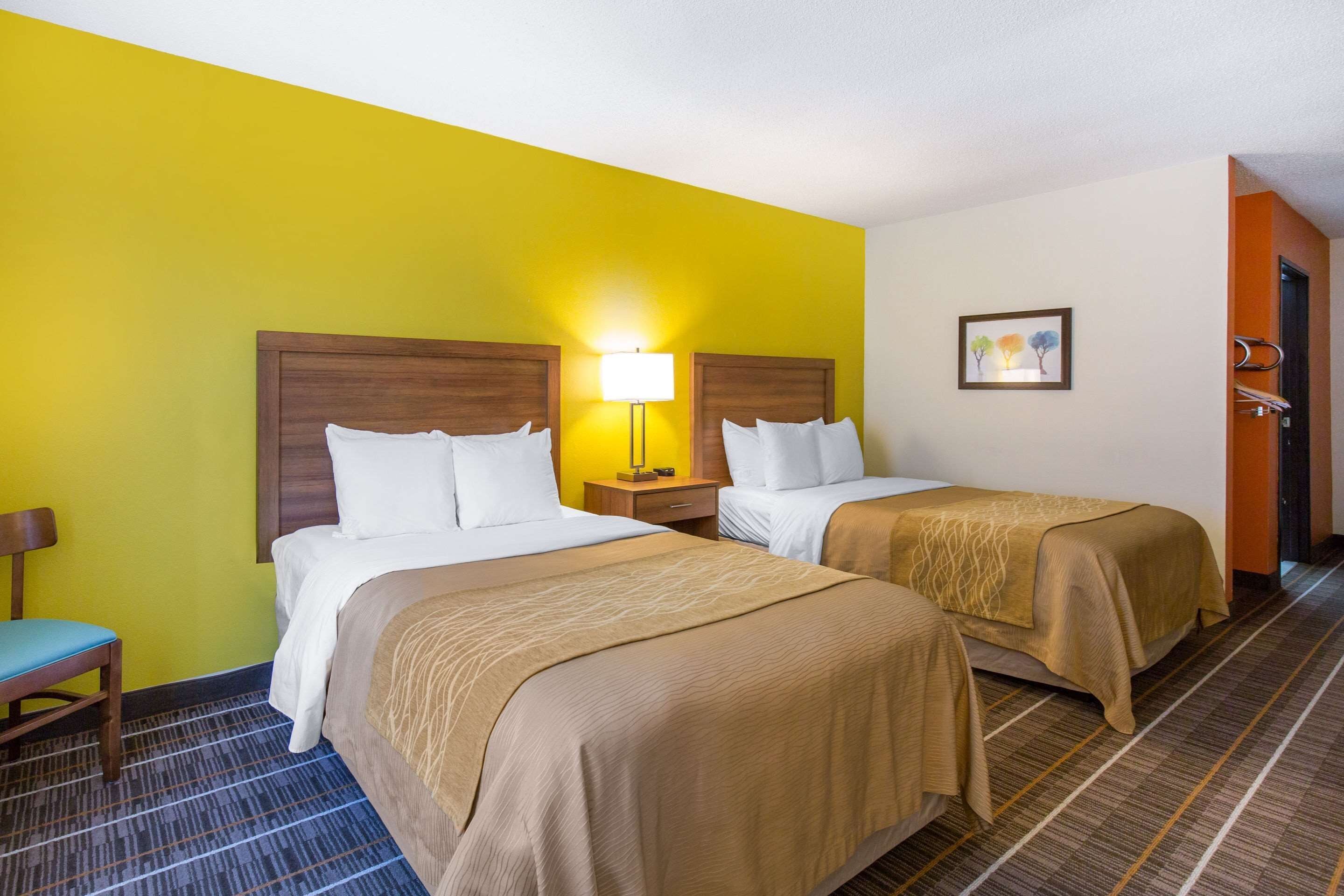 A hotel room with two beds, a nightstand, a chair, and a door.