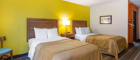 A hotel room with two beds, a nightstand, a chair, and a door.