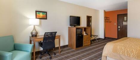 Una habitación de hotel con cama, escritorio con computadora, silla, lámpara, televisión y microondas.