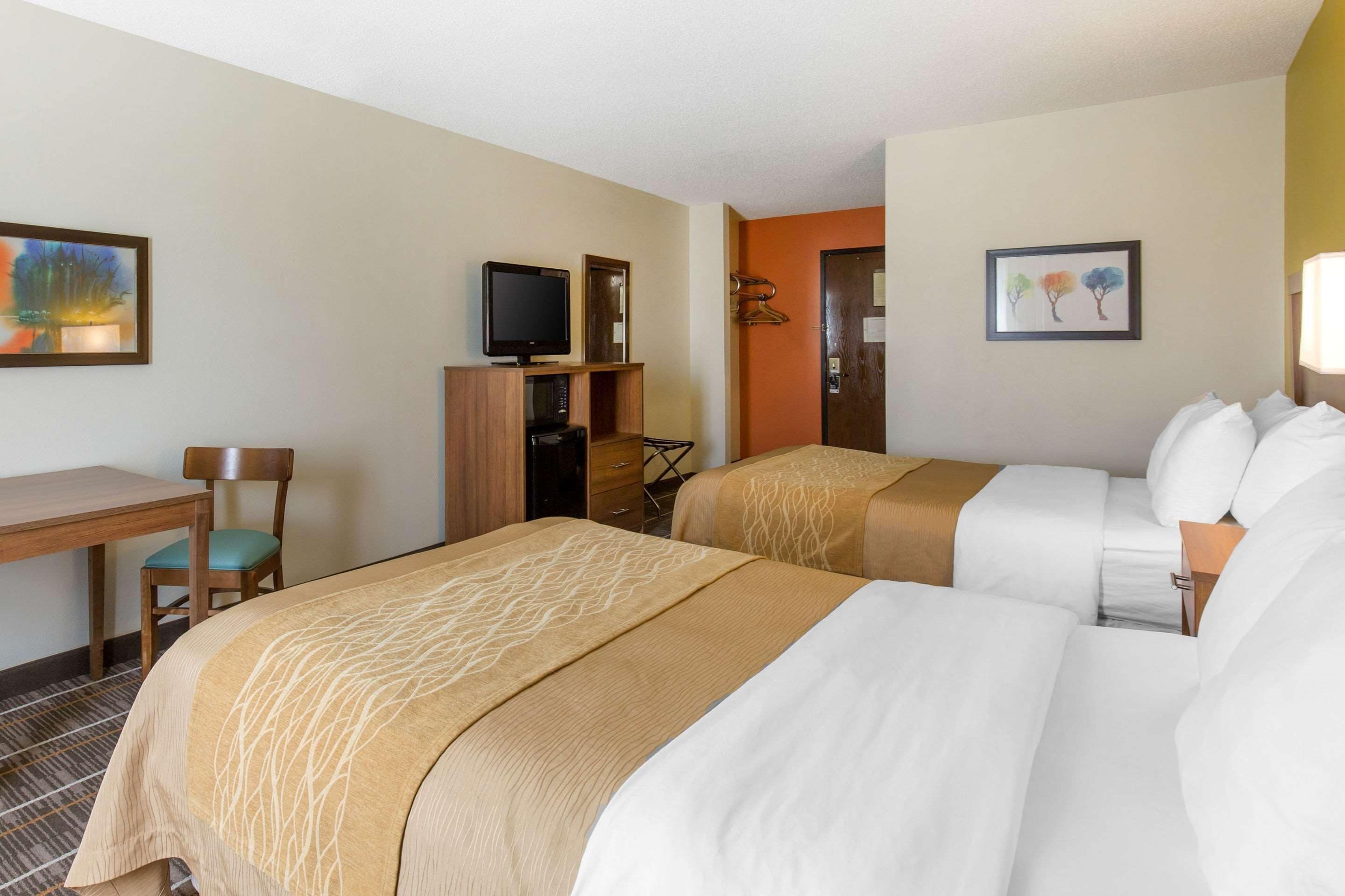 Una habitación de hotel con dos camas, un escritorio, una silla, un televisor y obras de arte en las paredes.