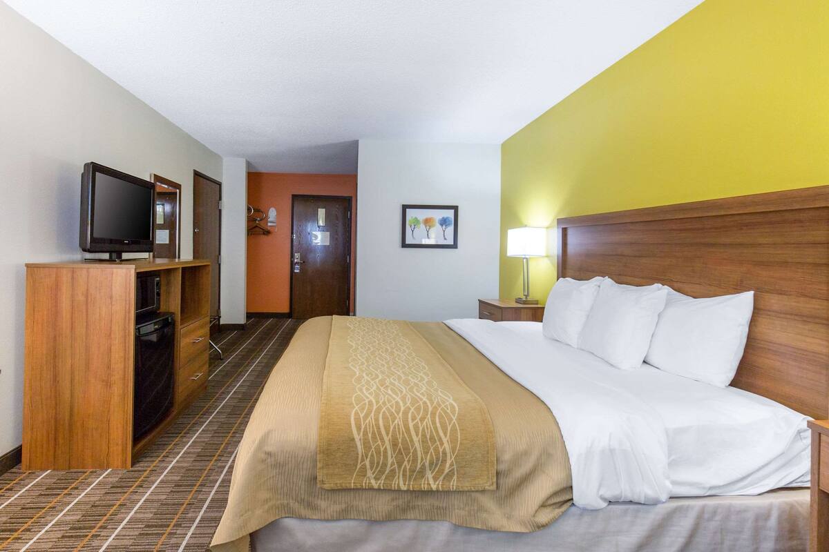 A hotel room with a bed, a TV on a wooden cabinet, a lamp, and a door leading to another room.