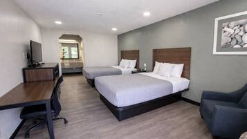 A hotel room with two beds, a desk, a chair, a TV, and a bathroom visible in the background.