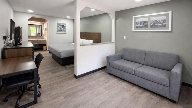 A modern hotel room with a desk, chair, grey sofa, two beds, and artwork on the walls. - Quality Inn Mt. Pleasant (Mount Pleasant)