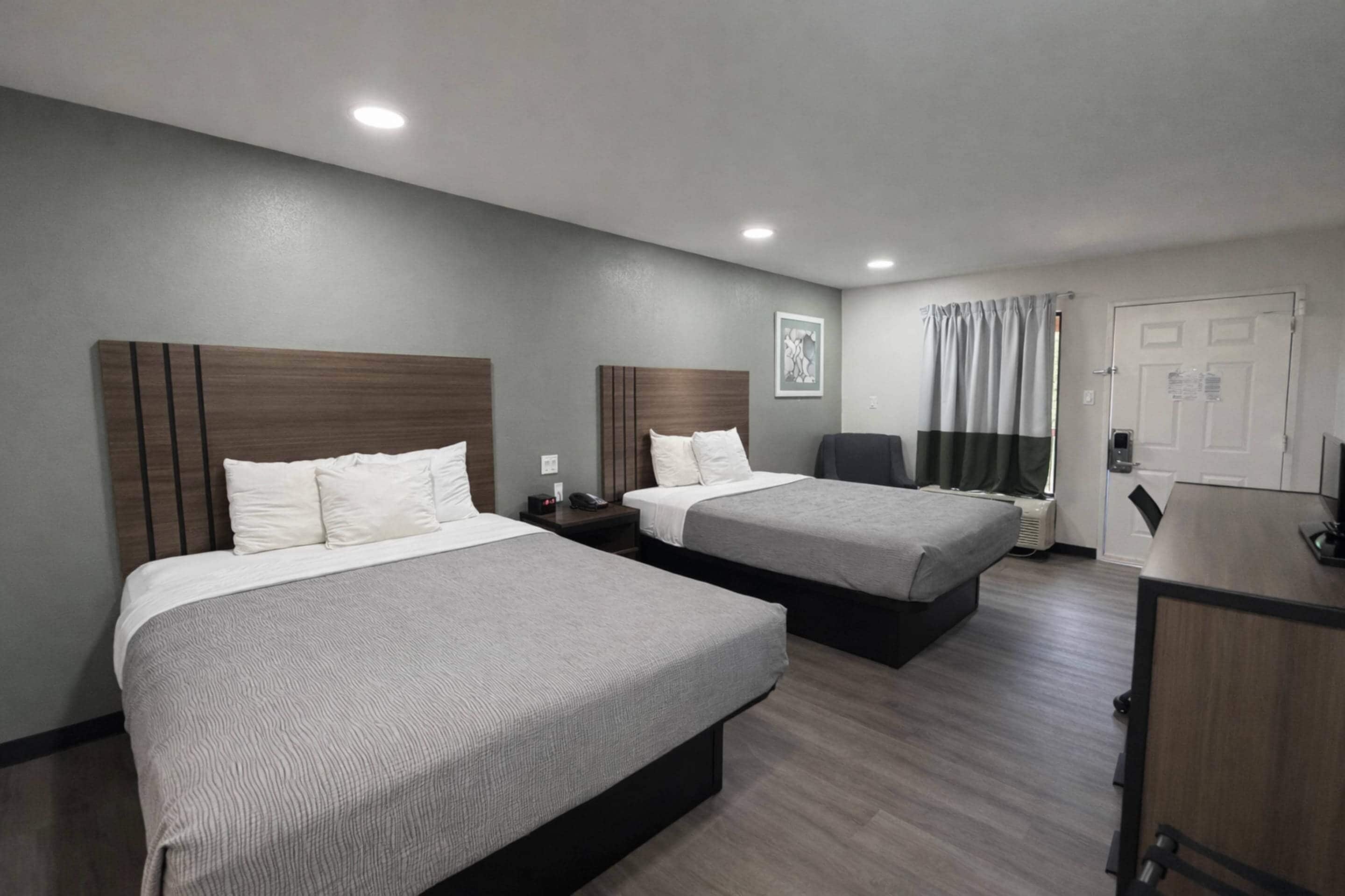 Une chambre d’hôtel avec deux lits, un bureau, une chaise et une porte.