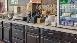 A breakfast counter with waffle makers, syrup dispensers, and a refrigerated display of dairy products. - Quality Inn Mt. Pleasant (Mount Pleasant)