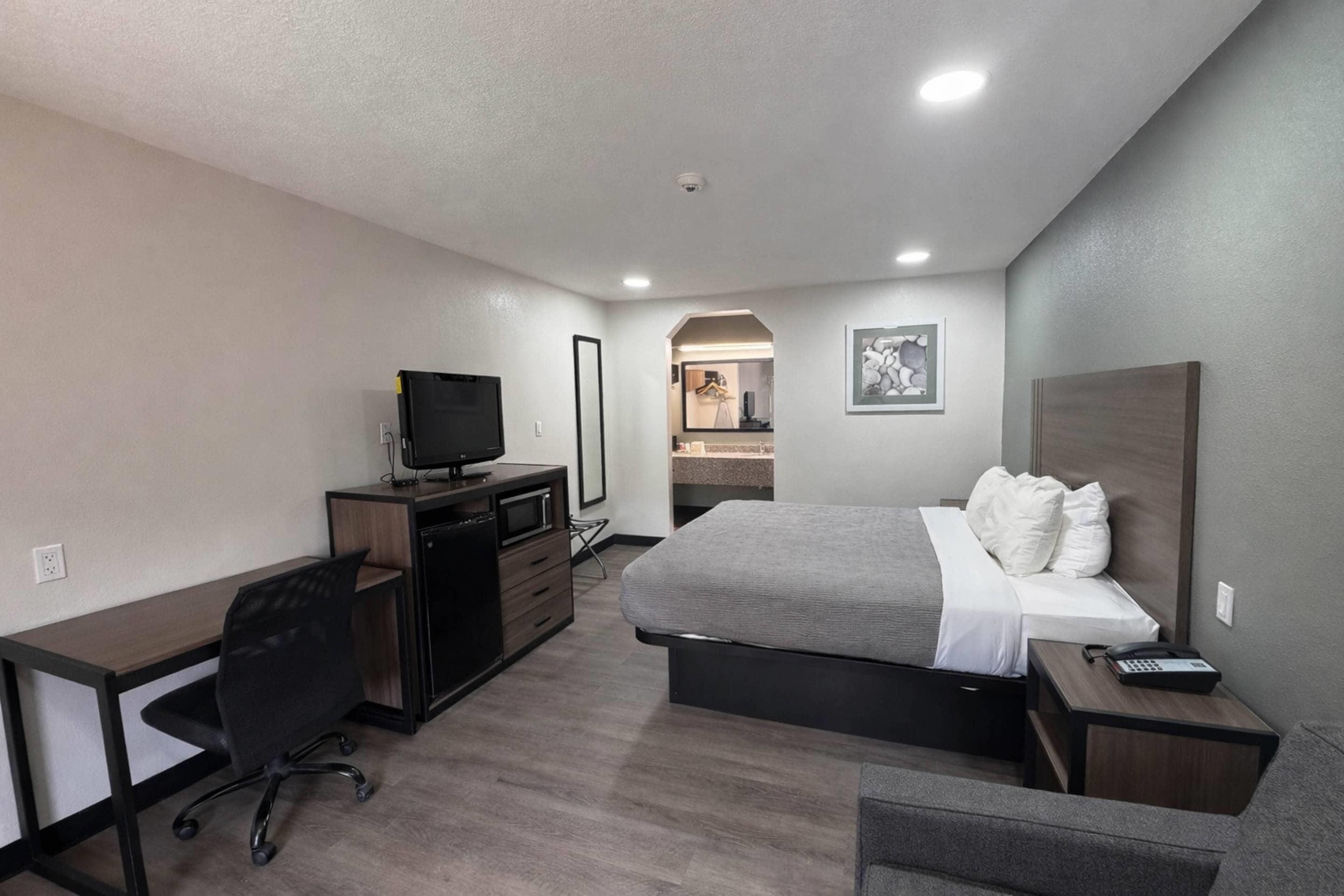 Una habitación de hotel con cama, escritorio, televisión, teléfono y espejo.