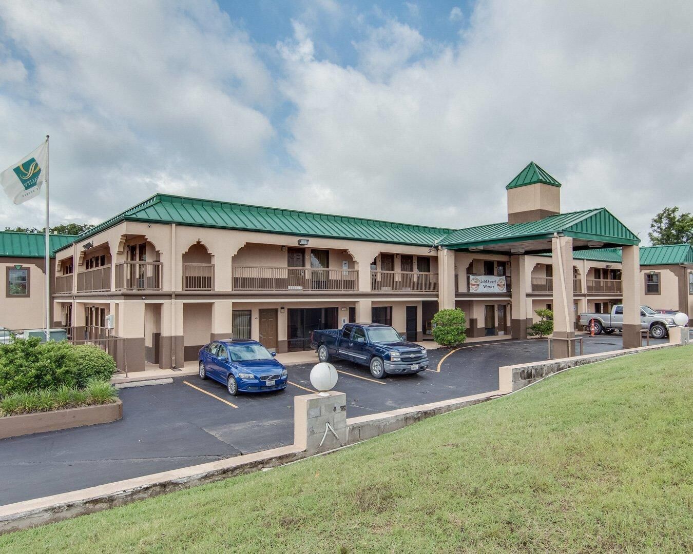 A hotel with a green roof, multiple balconies, and a parking lot.