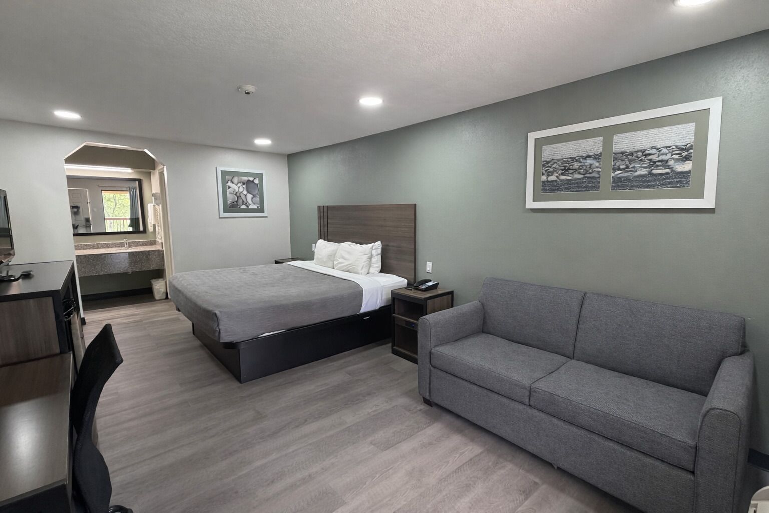Una habitació d'hotel amb un llit, un sofà gris, una taula de treball amb una cadira i una petita taula de nit.