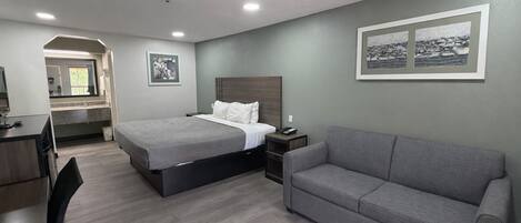 Una habitació d'hotel amb un llit, un sofà gris, una taula de treball amb una cadira i una petita taula de nit.