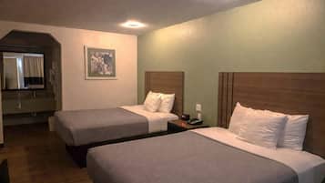 Habitación de hotel con dos camas, una mesita de noche con teléfono y un cuadro en la pared, además de un baño visible a través de un arco.