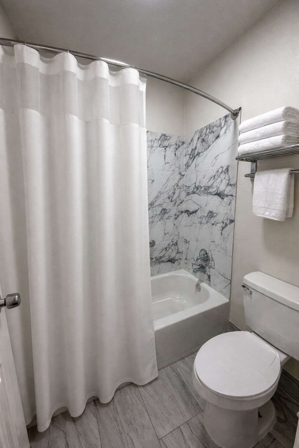A bathroom with a shower, a bathtub, a toilet, and a marble wall.