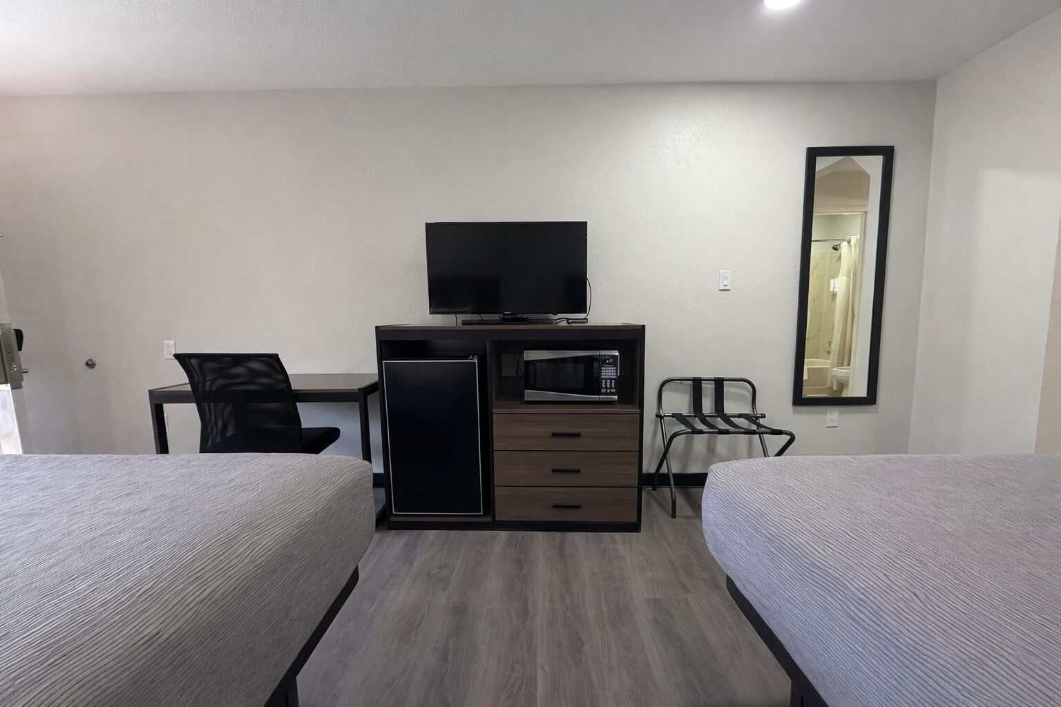 A hotel room with two beds, a desk with a chair, a TV, a microwave, and a mirror.