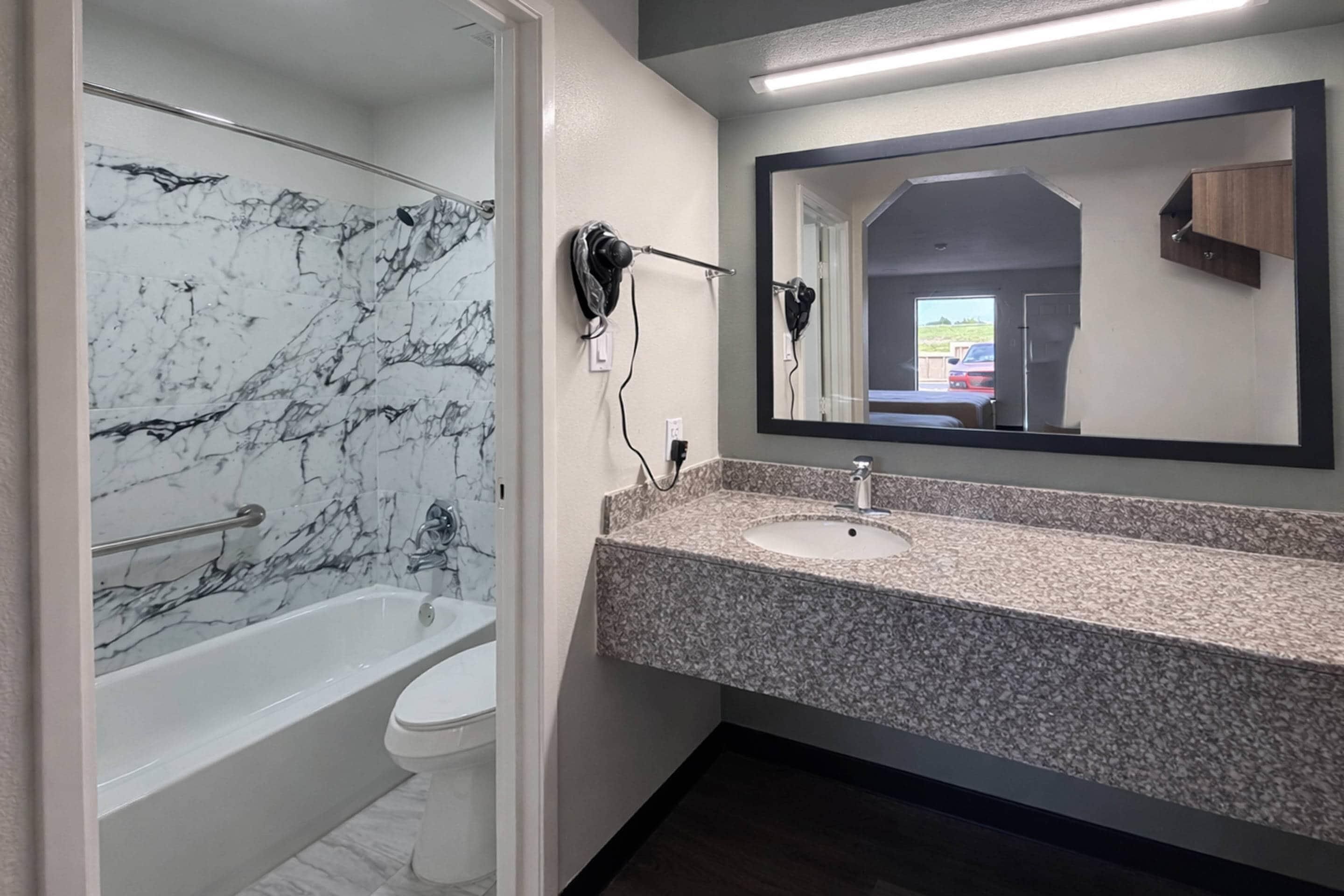 Un baño con pared de mármol, una bañera, un inodoro, un lavabo y un espejo.