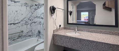 Un baño con pared de mármol, una bañera, un inodoro, un lavabo y un espejo.