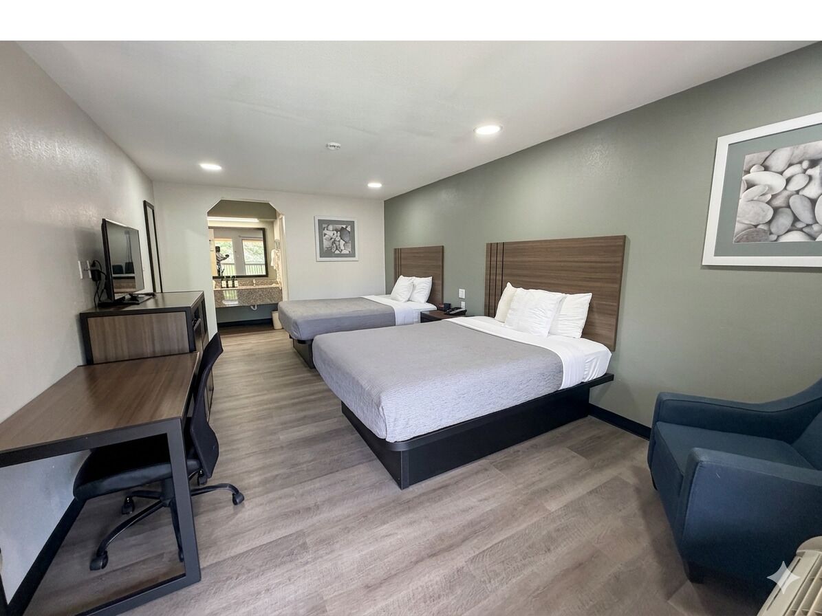 Une chambre d’hôtel avec deux lits, un bureau, une chaise et un téléviseur.