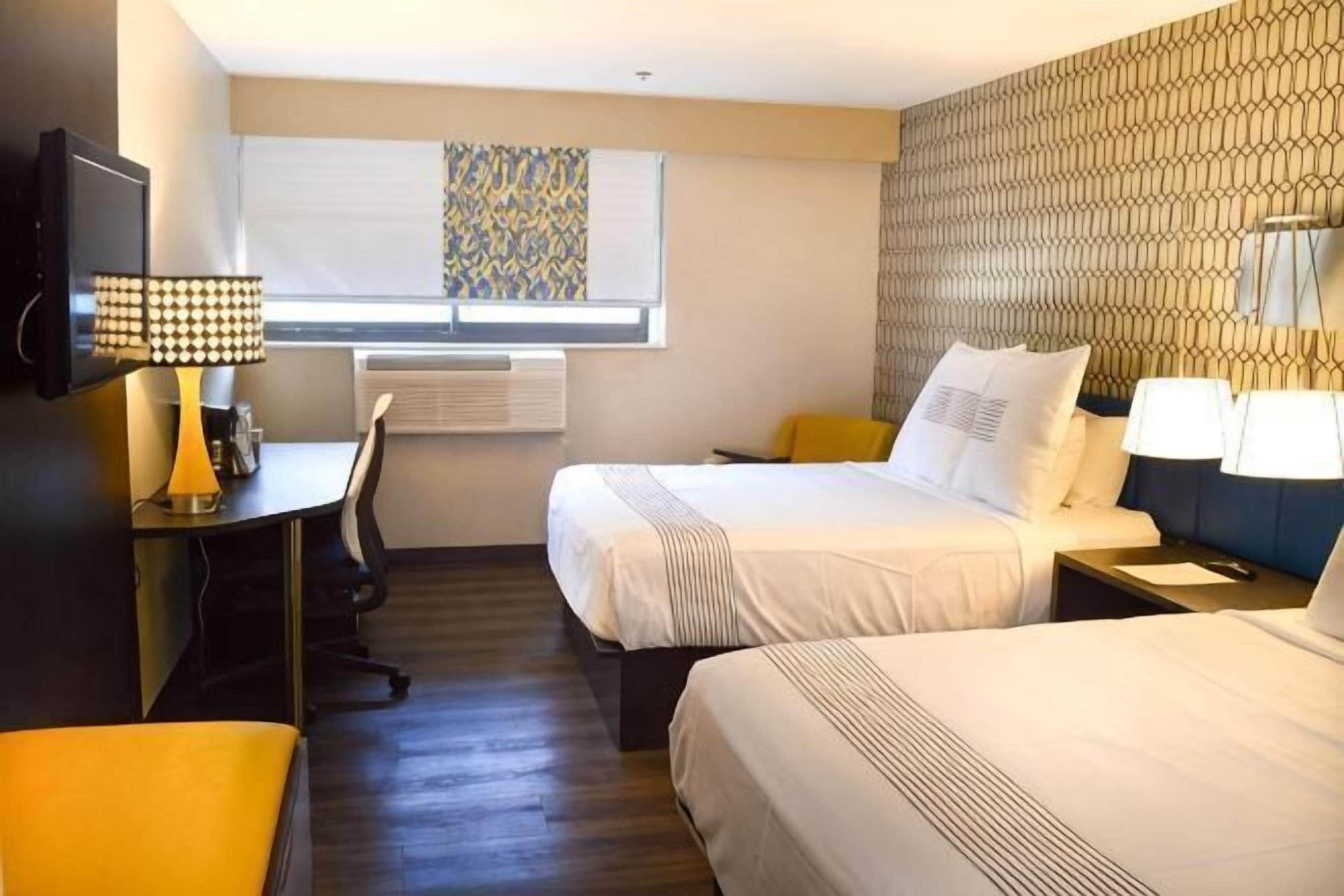 Habitación de hotel con dos camas, un escritorio, una silla, un televisor y una ventana con persianas.