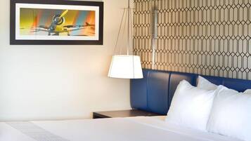 A hotel room with a bed, a nightstand, a lamp, and a wall-mounted artwork.