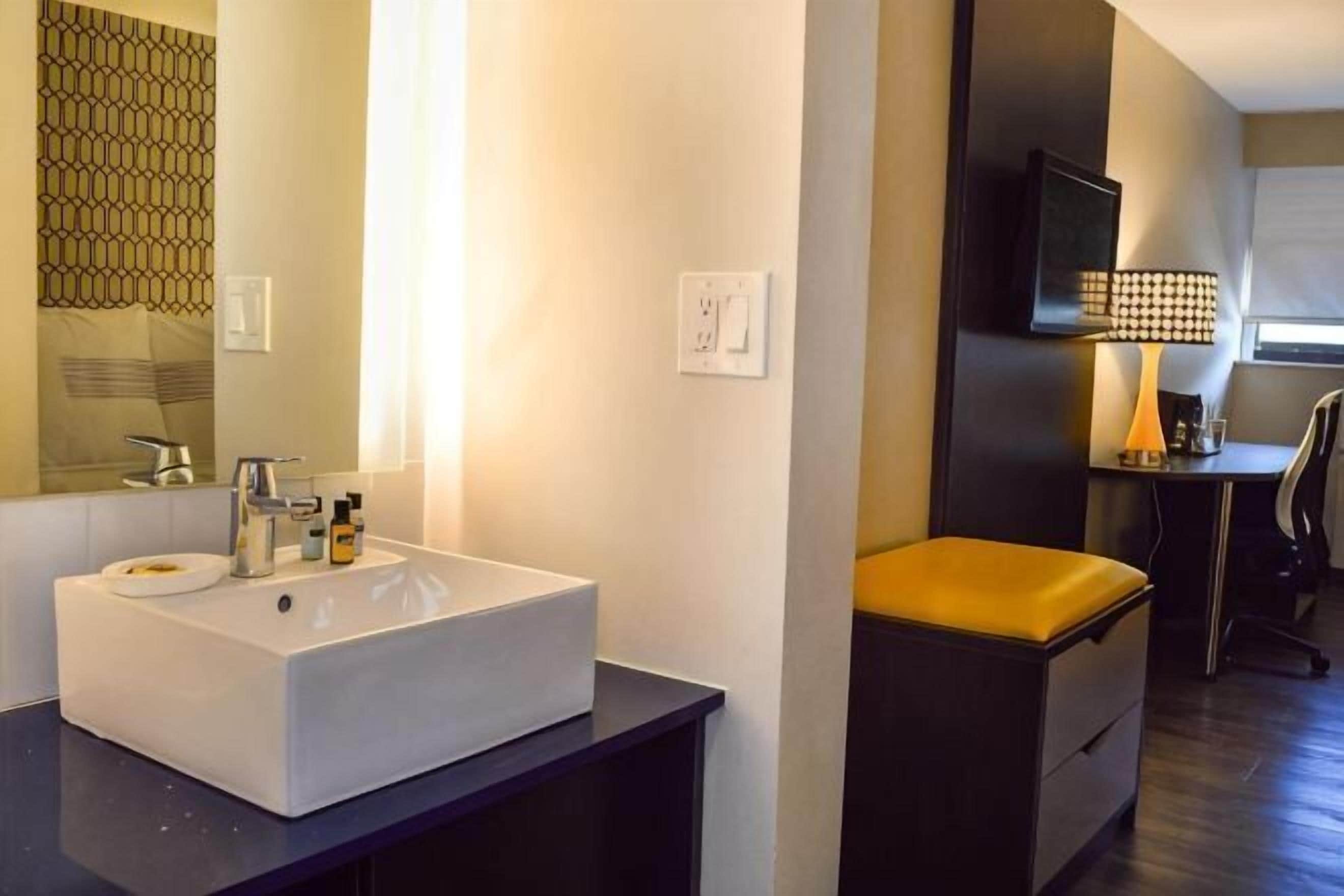 Un baño moderno con un lavamanos grande blanco, un espejo y una silla negra.