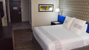 Habitación de hotel con cama, escritorio, mesita de noche, un cuadro en la pared y papel tapiz estampado.