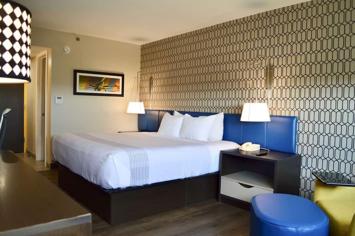 Camera d'albergo con un letto, comodini, una scrivania, una sedia, una lampada e una parete decorata.
