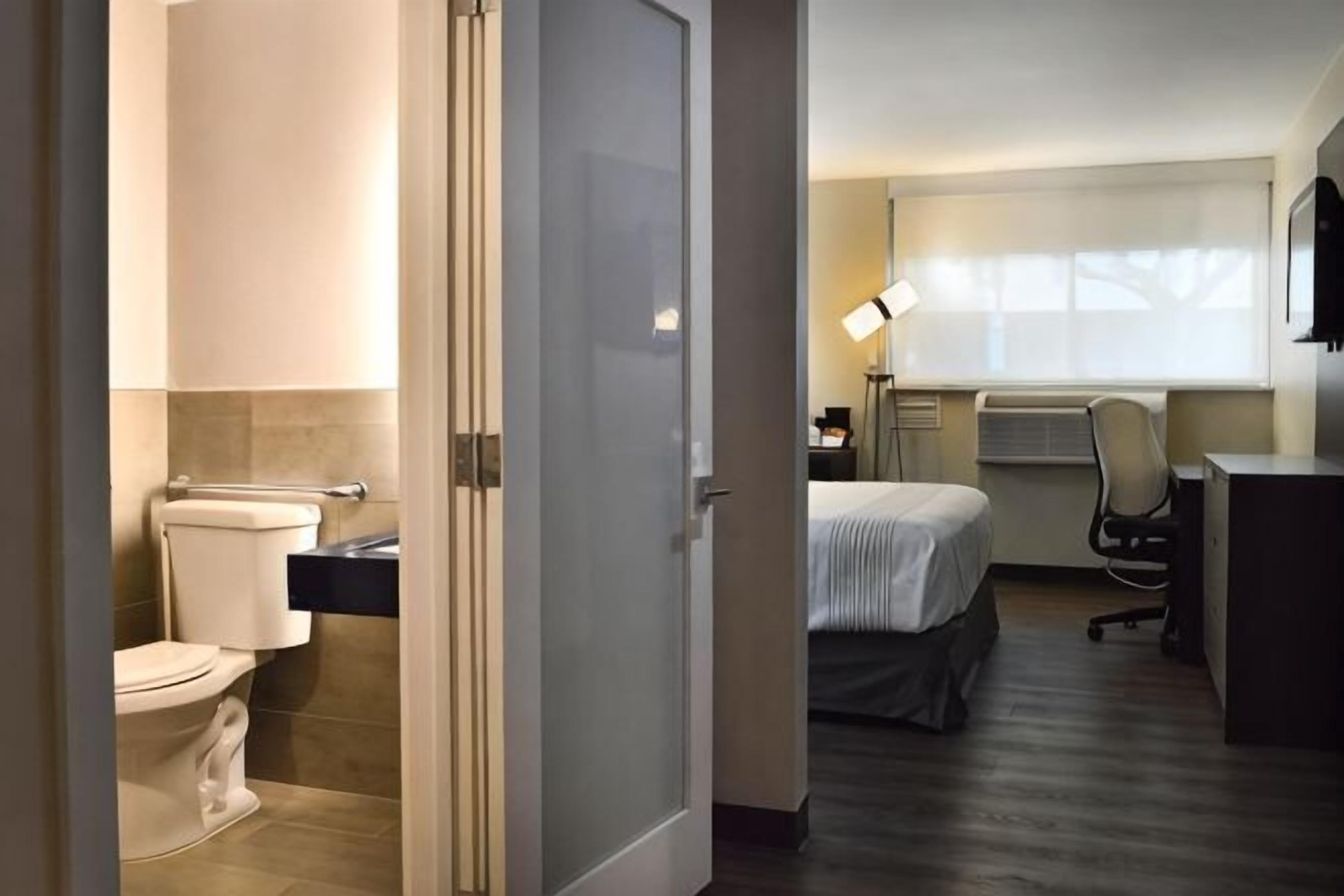 Habitación de hotel con inodoro, cama, escritorio y ventana.