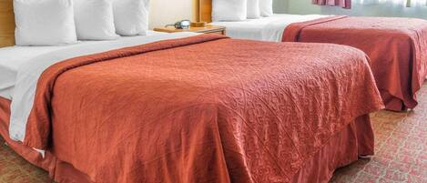 A hotel room with two beds, each with white bedding and a red blanket. There is a nightstand with a lamp and a telephone.