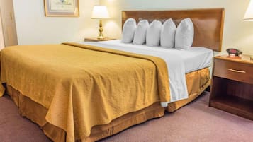 A hotel room with a large bed, a wooden headboard, two bedside lamps, a nightstand, and a framed picture on the wall.